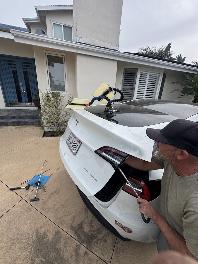 Technician working a paintless dent repair rod behind a Tesla Model Y tailgate