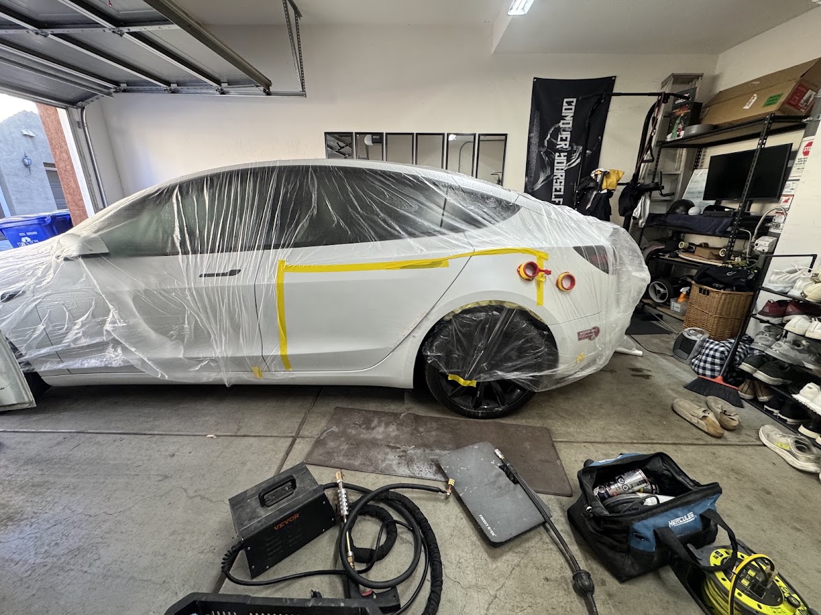 Dent pulling tabs and spot welder on a white Tesla Model 3 rear quarter