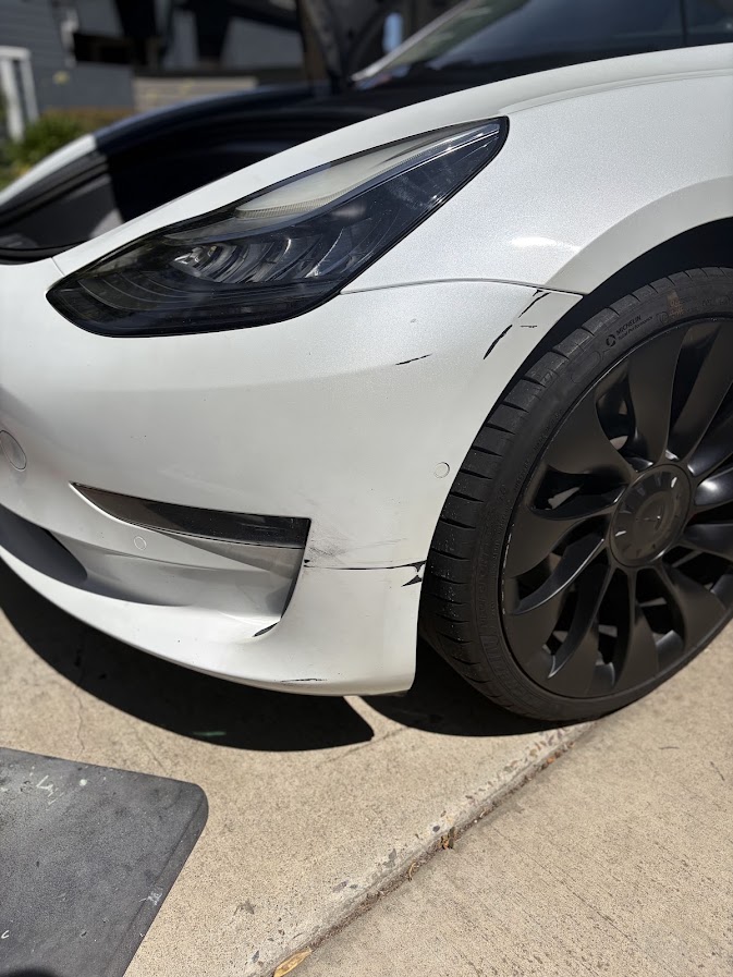 Black scrape marks on the front bumper of a white Tesla Model 3