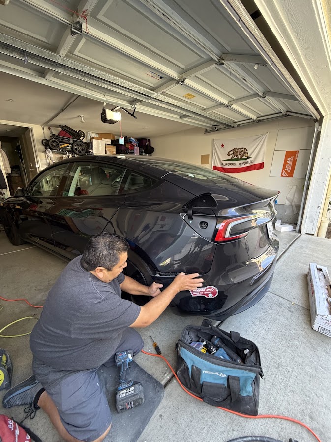 Technician fitting a rear bumper cover on a Midnight Silver Tesla Model 3