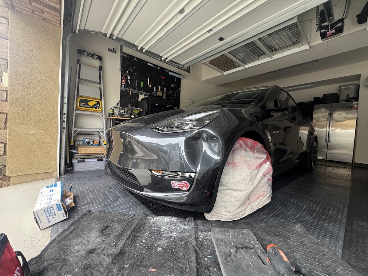 Dented front bumper on a Midnight Silver Tesla Model Y prepped for repair in a garage