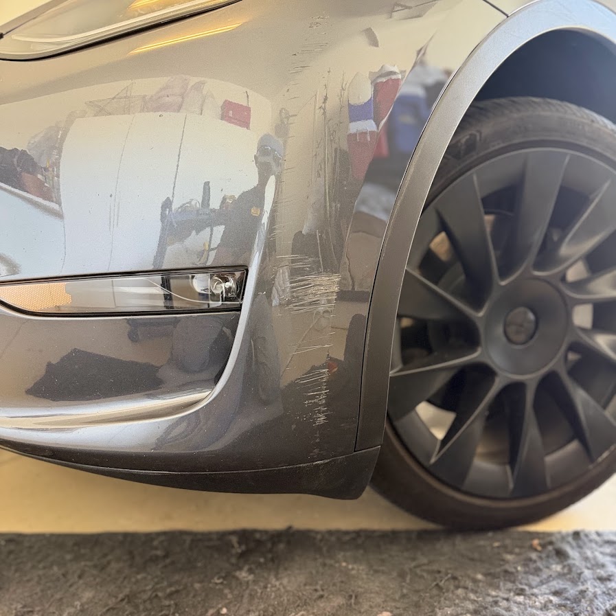 Midnight Silver Tesla Model Y front bumper with heavy scraping and a cracked fog light lens