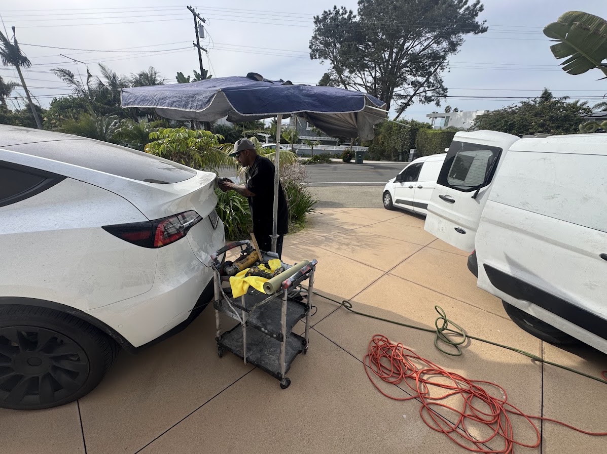 Technician working on a Tesla tailgate edge under an umbrella at a job site