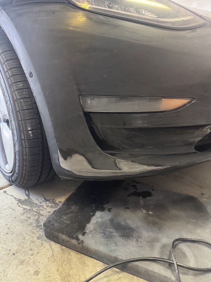 Sanded bumper corner prep on a black Tesla Model Y below the fog light