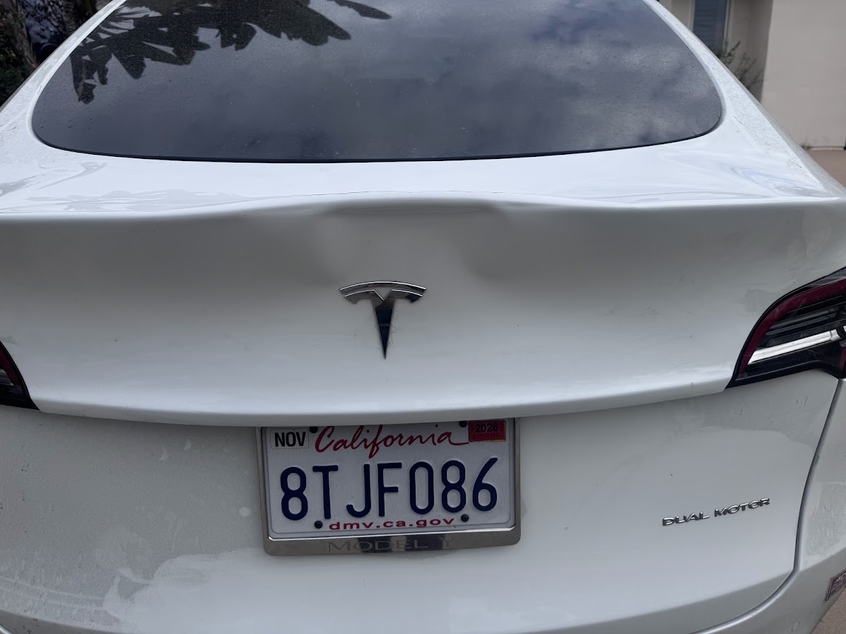 Crease dent on the tailgate of a white Tesla Model Y above the badge