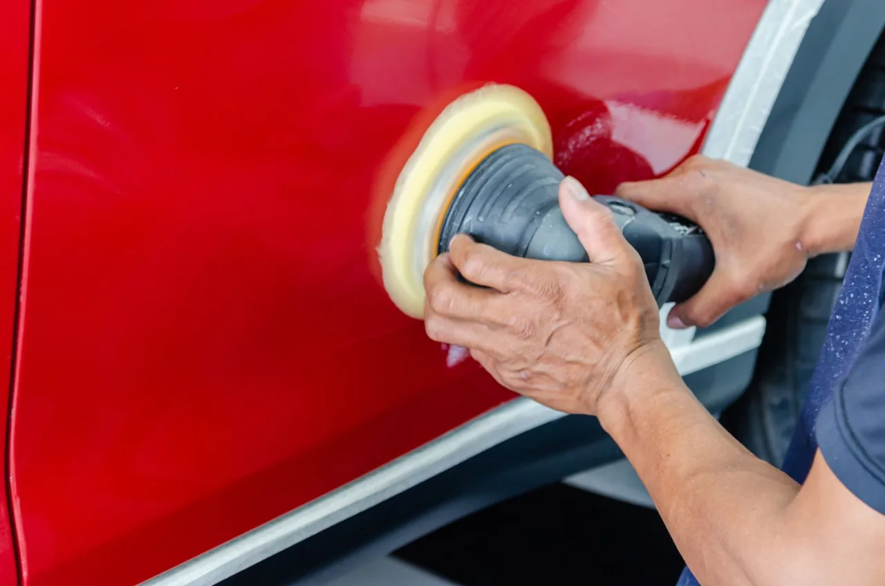 Worker machine-polishing a red vehicle side panel, an example of surface finish care — example stock photo, not BumperFixers work