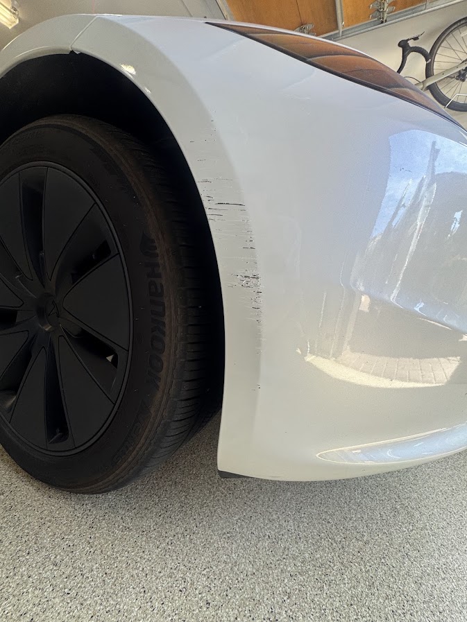 White Tesla Model 3 front bumper with black scrape marks ahead of the wheel arch