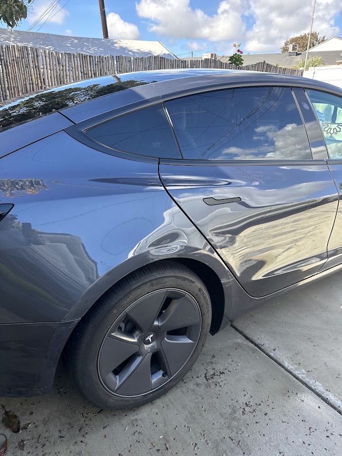 Dent and crease damage above the wheel arch on a Midnight Silver Tesla Model 3