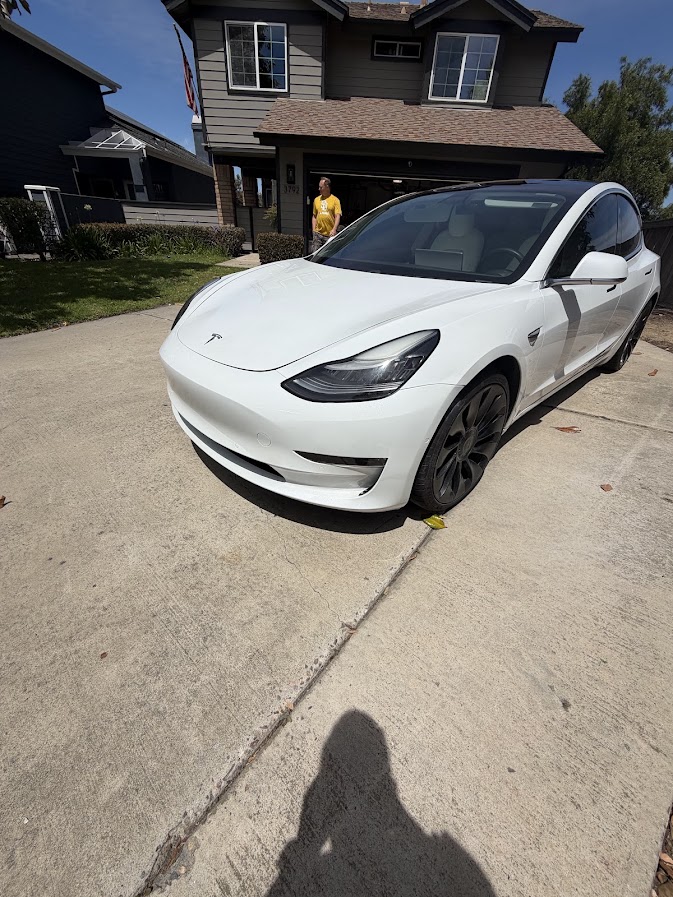 White Tesla Model 3 parked in a driveway with a scuffed front bumper