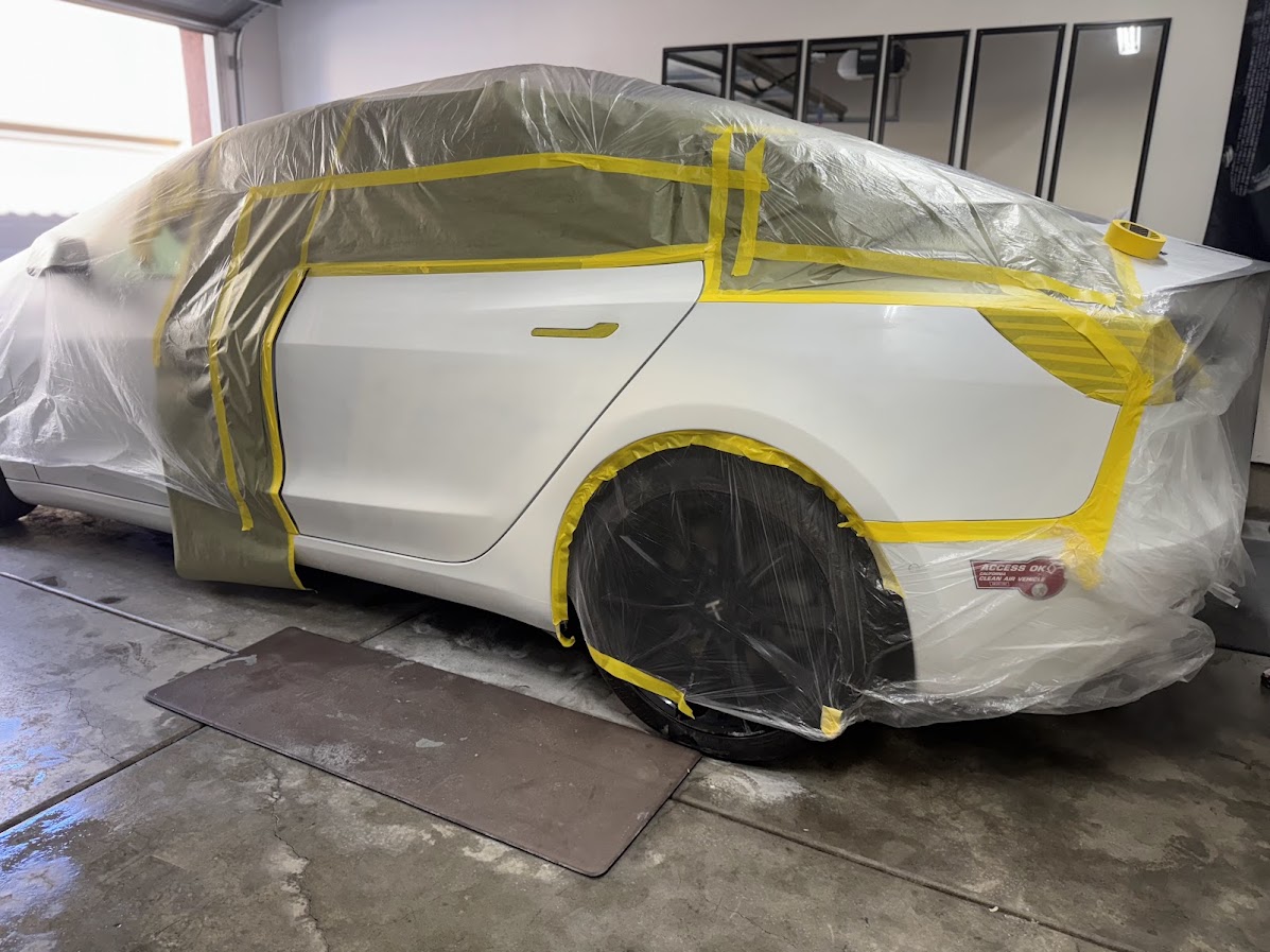 White Tesla Model 3 masked and sheeted for rear quarter paintwork