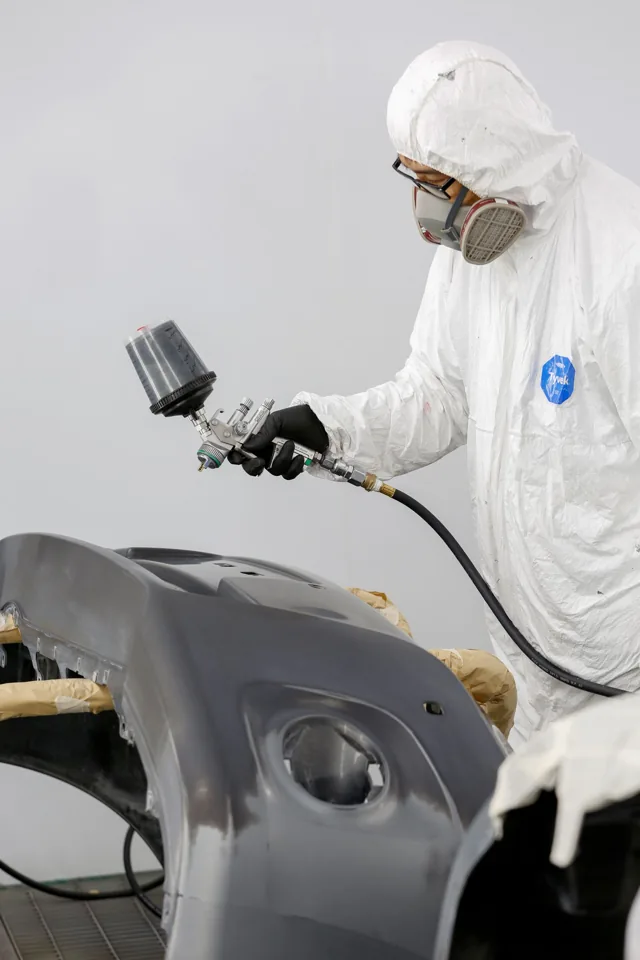 Technician spray-painting a detached bumper cover in a workshop — example stock photo, not BumperFixers work