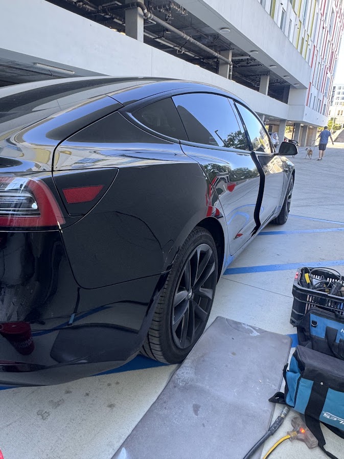 Black Tesla Model 3 at a mobile repair job site with tool bags and cords