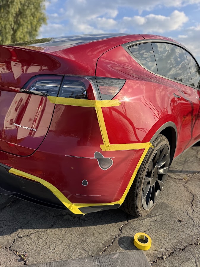 Red Tesla Model Y rear bumper corner sanded down to primer with masking tape in place